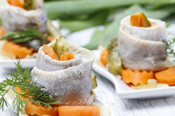 Pickled herring rolls with vegetables on wooden table