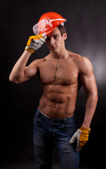 Muscular young man with an orange helmet on a black background.