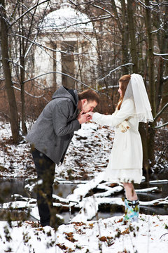 Groom kissing bride's hand in the winter woods
