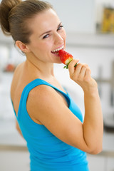 Portrait of happy young woman eating strawberry in kitchen