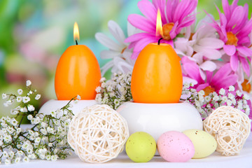 Easter candles with flowers on bright background