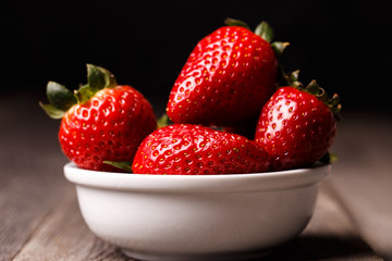 Strawberries in white plate on the old wooden table.