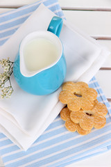 Blue jug with milk and cookies on wooden picnic table close-up