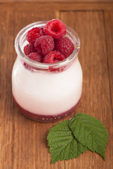 White yogurt in a glass jar with raspberry on wooden boards