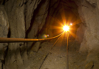 Inside abandoned gold mine with shining gold light and ore cart tracks.