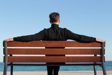 Dark dressed man relaxing on a bench in the sund