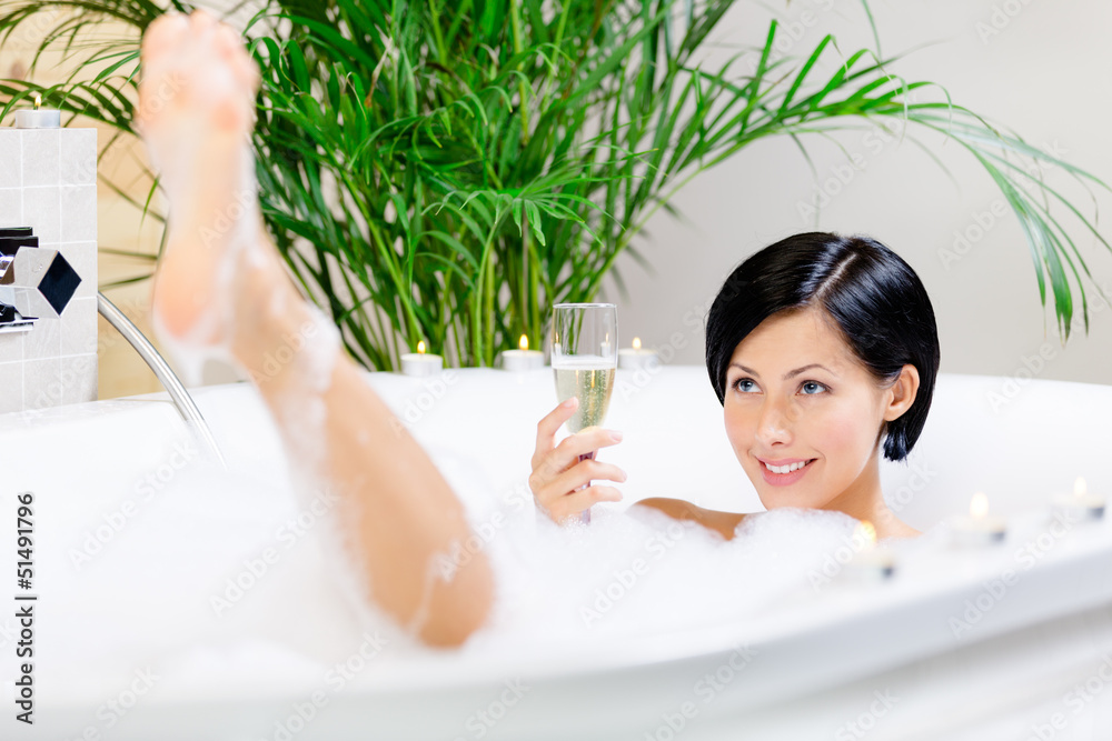 Wall mural Woman taking a bath with suds drinks champagne