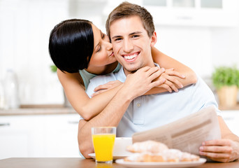 Obraz na płótnie Canvas Girl kisses eating boyfriend who sits at the kitchen table 