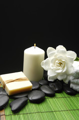Fototapeta na wymiar Gardenia and stones with soap, towel and candle on green mat