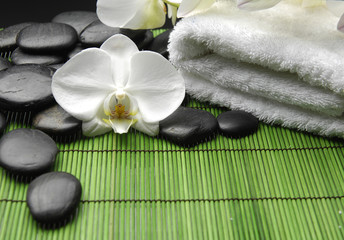 Fototapeta na wymiar White orchid and stones with white towel on green mat