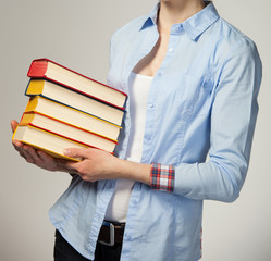 Unrecognizable girl holding a stack of books; grey background