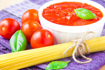 Italian tomato sauce in a white cup with uncooked spaghetti