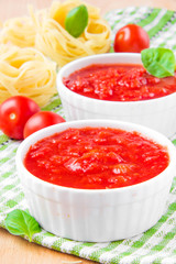 Italian tomato sauce in a white cup with raw pasta, basil and ch