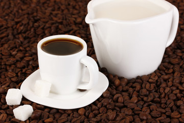 A cup of strong coffee and sweet cream on coffee beans close-up