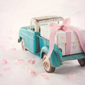 Old antique toy truck carrying a gift box with pink ribbon