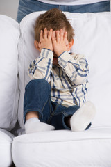 Portrait of little boy closing eyes with his hands at home
