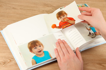 Photos in hands and photo album on wooden table