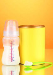 Bottle with milk and food for babies on orange background