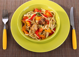 Noodles with vegetables on plate on wooden mat close-up