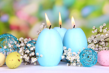 Easter candles with flowers on bright background