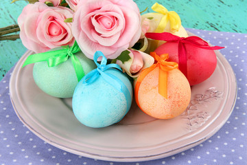 Easter eggs on plate with napkin and flowers on wooden table
