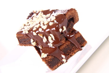 Slices of a brownie on a plate covered with chocolate and nuts