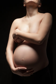 Close-up of pregnant woman touching her belly, isolated on black