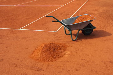 Wheelbarrow filled with red clay, on the tennis court