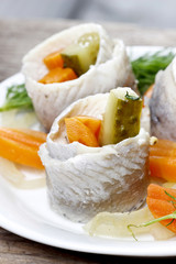 Pickled herring rolls with vegetables on wooden table