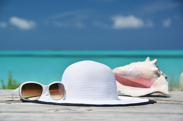 Sunglasses, hat and conch against ocean. Exuma, Bahamas
