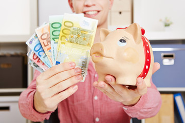 Hände halten Euro-Geldscheine und Sparschwein
