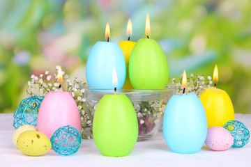 Easter candles with flowers on bright background