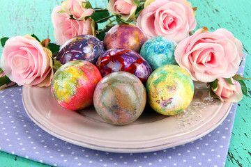 Easter eggs on plate with napkin and flowers on wooden table