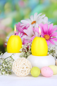 Easter candles with flowers on bright background