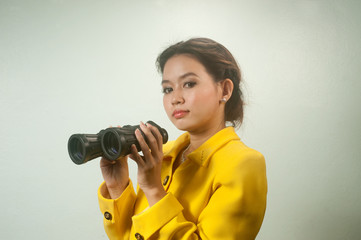 Pretty young Asian businesswoman in yellow suit holding a binocu