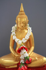 Golden Buddha statue with garland ob gray background
