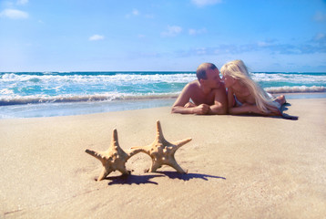 Obraz na płótnie Canvas loving couple lying on the sea sand beach against starfishs and