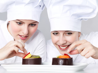 Two female chef bakers in uniform tasting a dessert