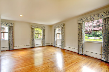 Large empty room with hardwood floor and curtains.