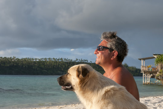 Dog And Man On Tropical Paradise White Sand Beach Sunset