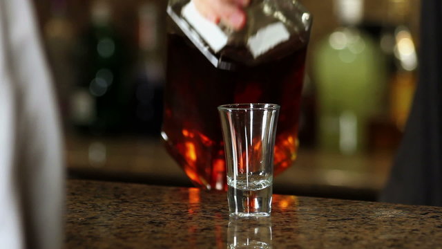 A bartender pours some whiskey into a shot glass for a customer.
