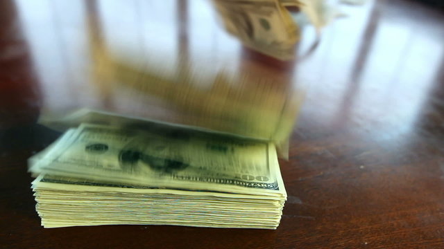 A large stack of hundred dollar bills on a table gradually blows away to nothing.