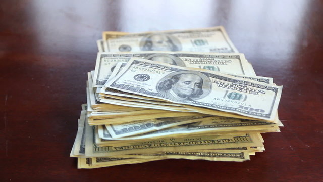 Hundred dollar bills falling into a stack on a table.