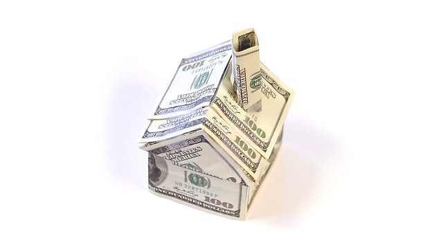 A small house made of hundred dollar bills rotates around over a white background.