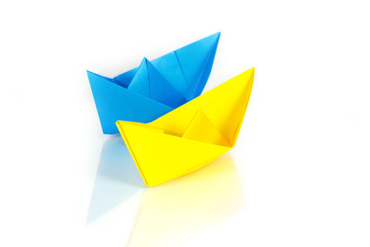 Blue and yellow paper ships on a glass with reflection