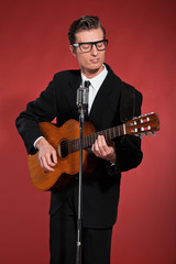 Retro fifties singer with glasses playing acoustic guitar. Studi