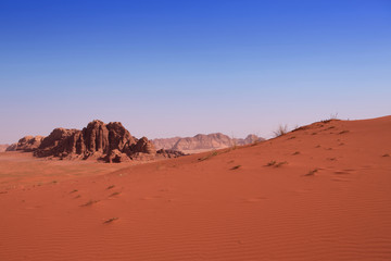 Fototapeta na wymiar Czerwone wydmy na tle skały w pustyni Wadi Rum