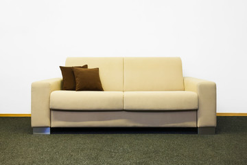 Beige modern sofa with brown cushions before white wall