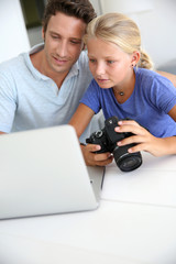 Father and daughter looking at digital camera and laptop