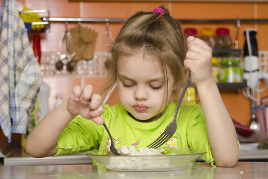 Четырехлетняя девочка ест вилкой и ложкой сидя за столом